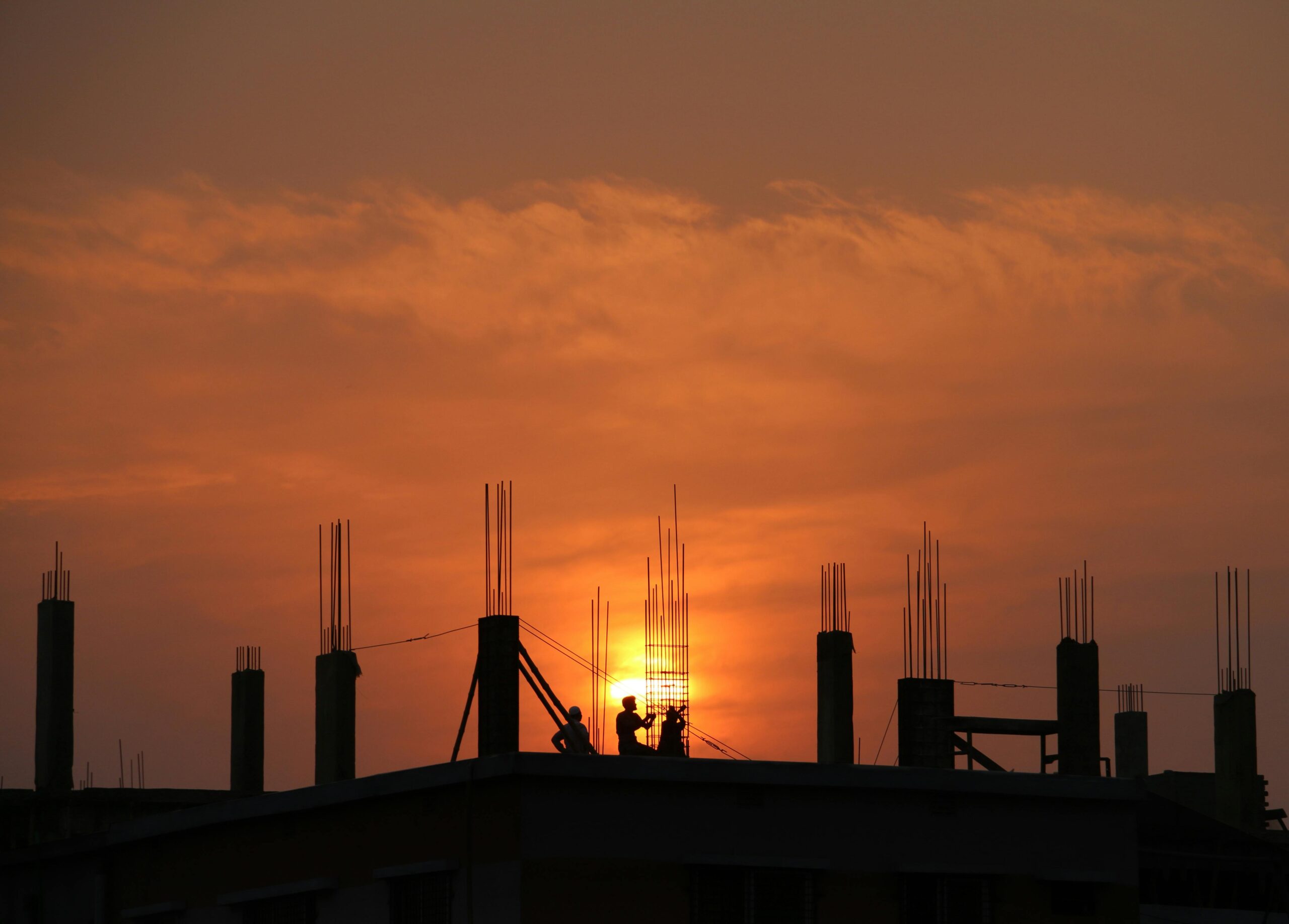 pexels-photo-176342-176342-1 Silhouette of workers on a construction site against a vibrant sunset sky.